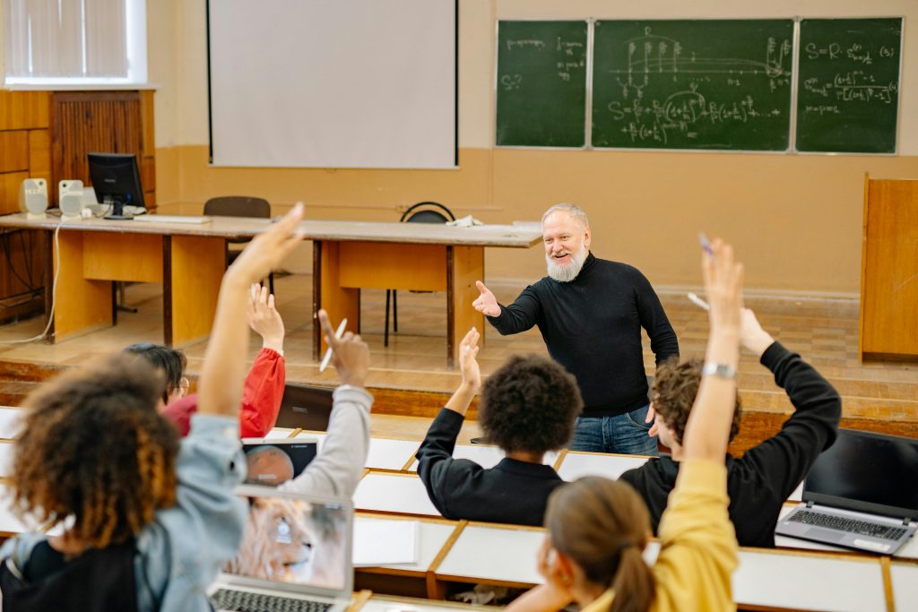 Instructor in classroom looking at students raising their hands to answer a question.